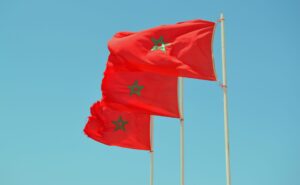 Three flags of Morocco are flying in the wind next to each other on a blue sky background.