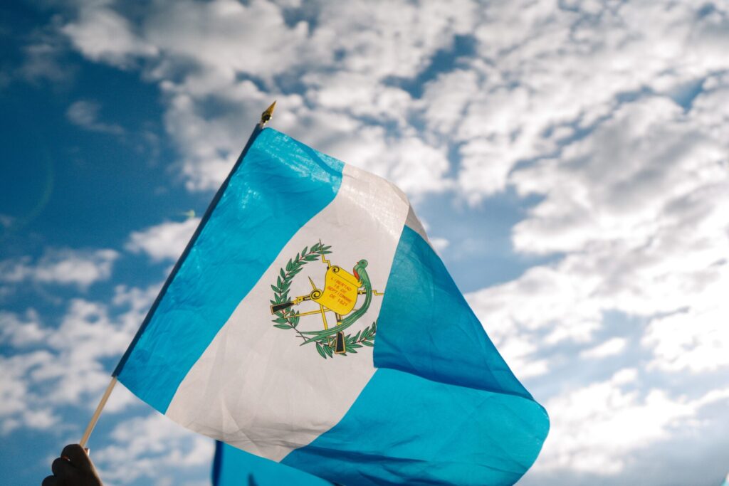 The flag of Guatemala flying under a cloudy and sunny sky