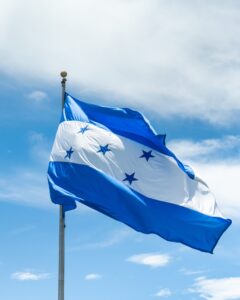 The flag of Honduras flying in the wind against a cloudy blue sky background.
