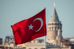 The flag of Turkey flying with an old building in the background