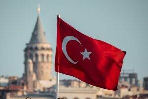 The flag of Turkey flying with an old building in the background