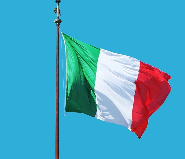 The Italian flag blowing in the wind against a blue sky. The flag is composed of three horizontal stripes, the first green, the second white and the third red.