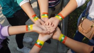 A group of hands joined together with Myanmar flag painted on the wrists