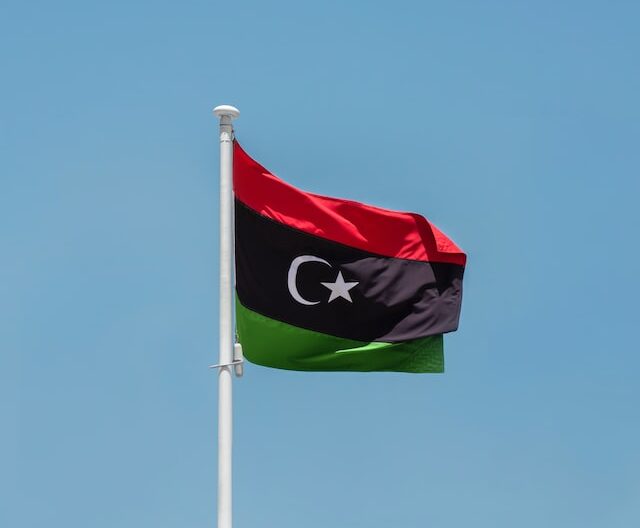 The flag of Libya flying in the wind against a blue sky background.