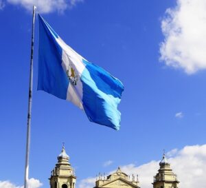 The flag of Guatemala blowing in the wind from the top of a flagpole, outdoors