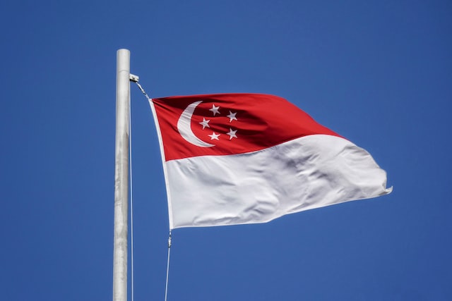 The flag of Singapore is at full-mast blowing in the wind against a blue sky background.
