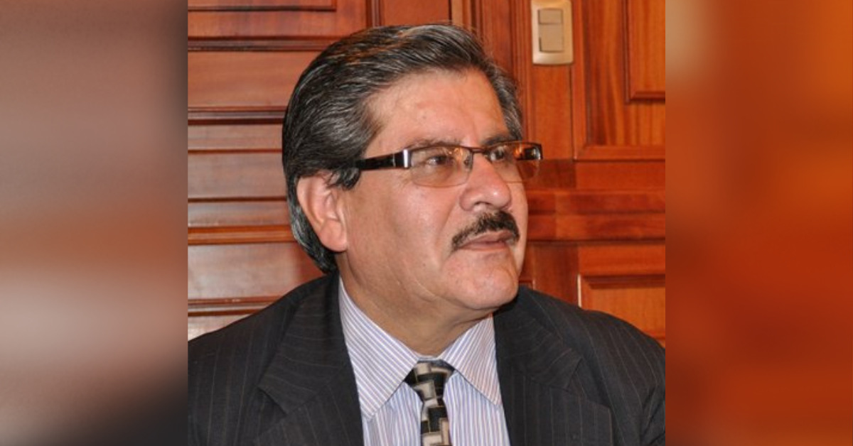 Portrait photo of Waldo Albarracín Sánchez. He is wearing a dark grey suit with a black and white tie and a thinky striped shirt. He is wearing some glasses.