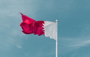 The flag of Qatar flying against a blue sky background.