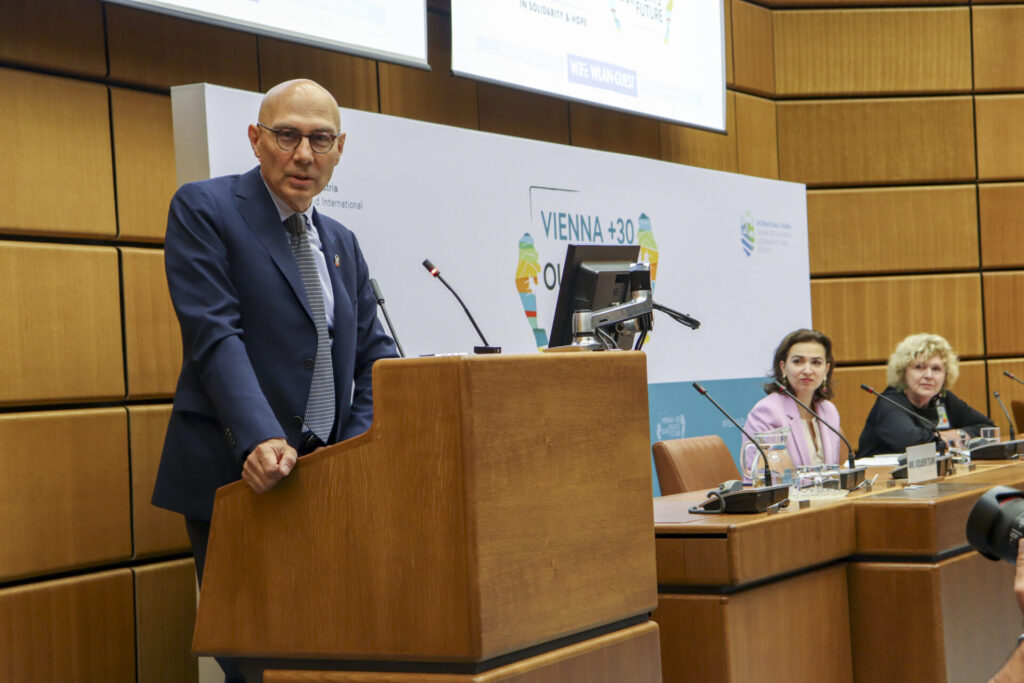 UN High Commissioner for Human Rights Volker Türk is standing at a lectern and looking straight into the camera while delivering a statement at the start of the 2023 Vienna Youth & Child Human Rights Defenders Conference. Seated to his left are Austrian Minister of Justice Alma Zadić and UN Special Rapporteur on Human Rights Defenders Mary Lawlor. 