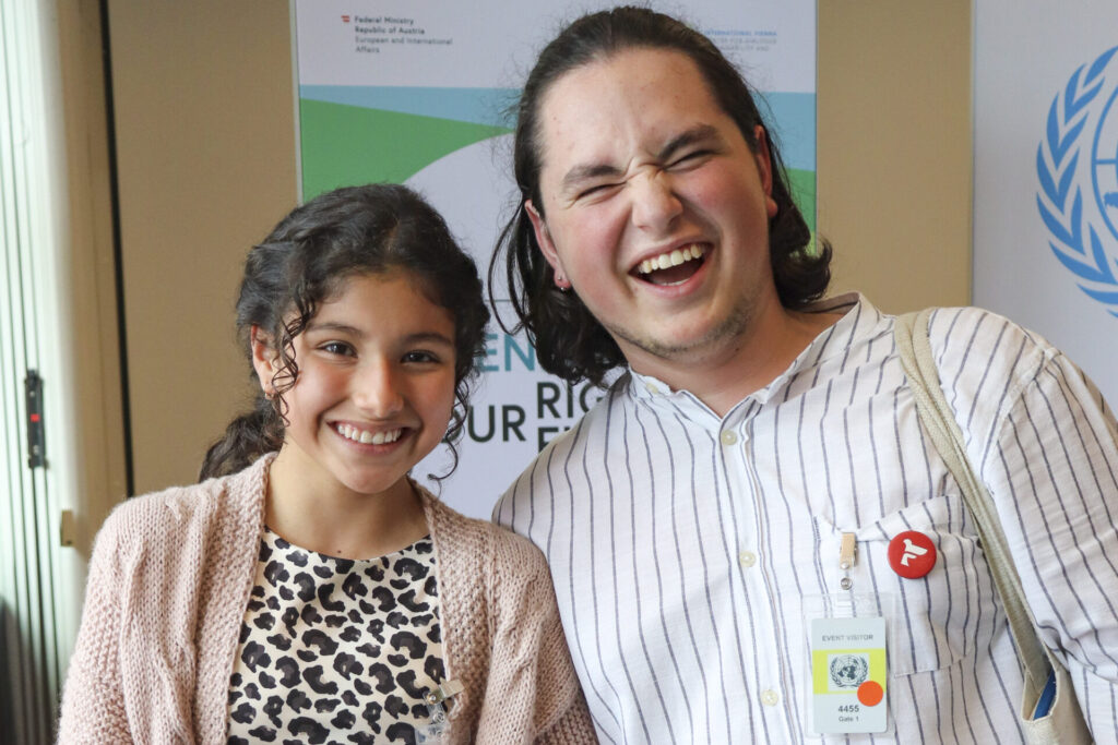 A close-up shot of young human rights defenders Dulce from Ecuador, and Vasile from Moldova, laughing together while looking at the camera. 