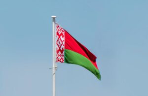 The flag of Belarus flying at the top of a pole against a blue sky background.