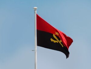 The flag of Angola flying in the wind, on a blue sky background.