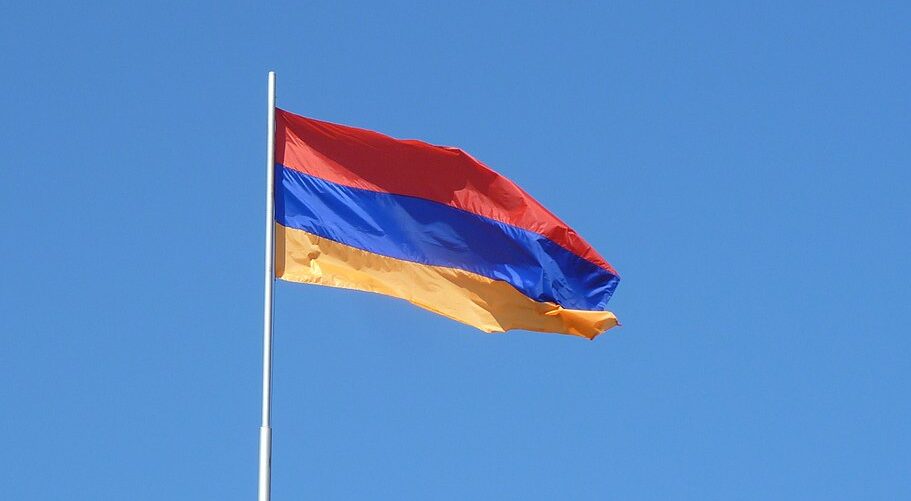 The flag of Armenia flying in the wind against a blue sky background.