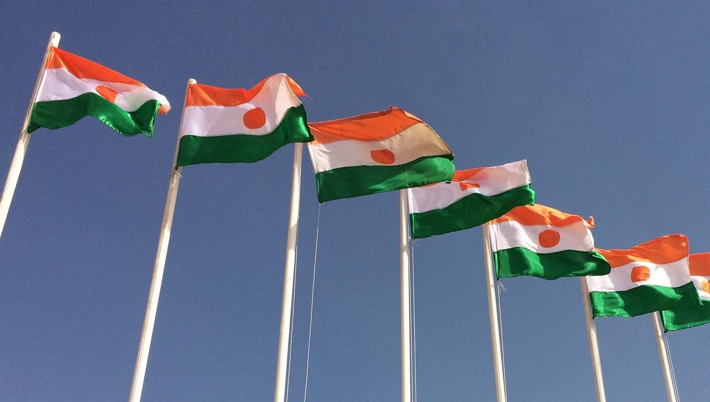 Seven flags of Niger on top of flagpoles, flying in the wind.