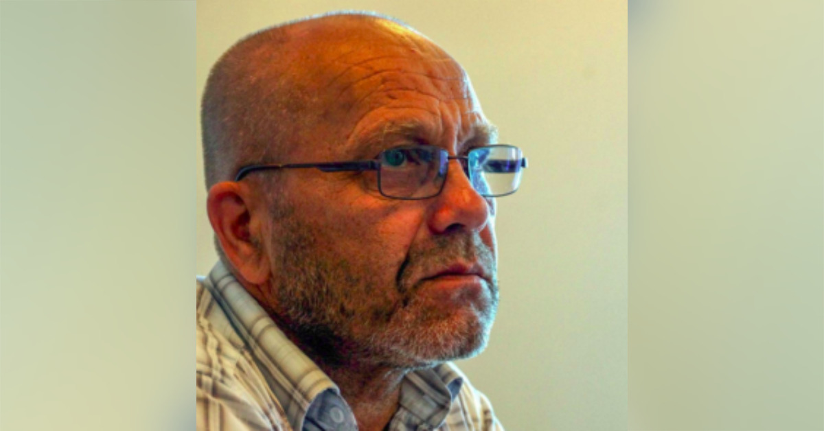 A close up photo of human rights defender Abdureshit Dzhepparov looking to the right with a serious demeanor. He is wearing glasses, a check shirt and has very short grey hair and stubble beard.