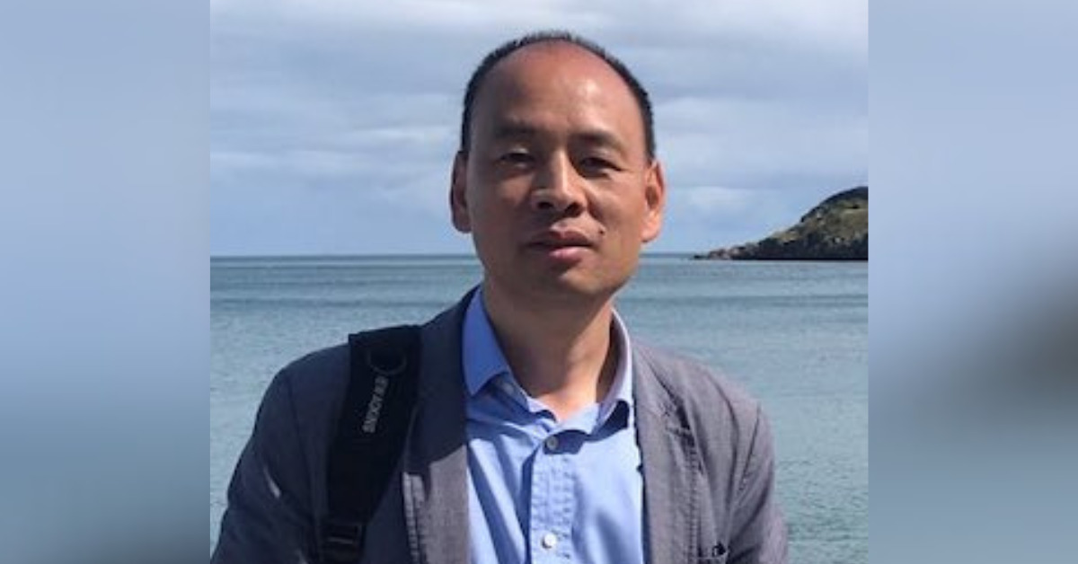 A close-up of Chinese human rights lawyer Lu Siwei standing outdside, with the sea in the background. He is wearing a light blue shirt and a grey jacket.