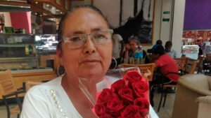 Mexican human rights defender Teresa Magueyal is sitting at a café indoor. She is holding a bouquet of red roses.