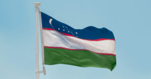 The flag of Uzbekistan flying in the wind against a blue sky background.