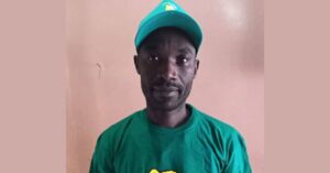 Human rights defender Obedi Karafuru looking straight at the camera. He is standing against a pink wall and wearing a green cap and T-shirt.