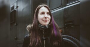 A portrait photograph of Nasta Loika before her arrest. She is looking to the side of the camera and has long brown hair, with a streak dyed purple. She is wearing a black winter coat.