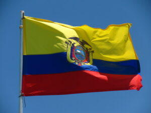 The flag of Ecuador flying in the wind under a blue sky.