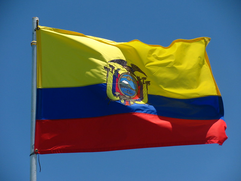 The flag of Ecuador flying in the wind under a blue sky.