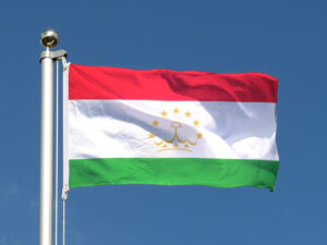 The flag of Tajikistan flying in the wind under a blue sky.