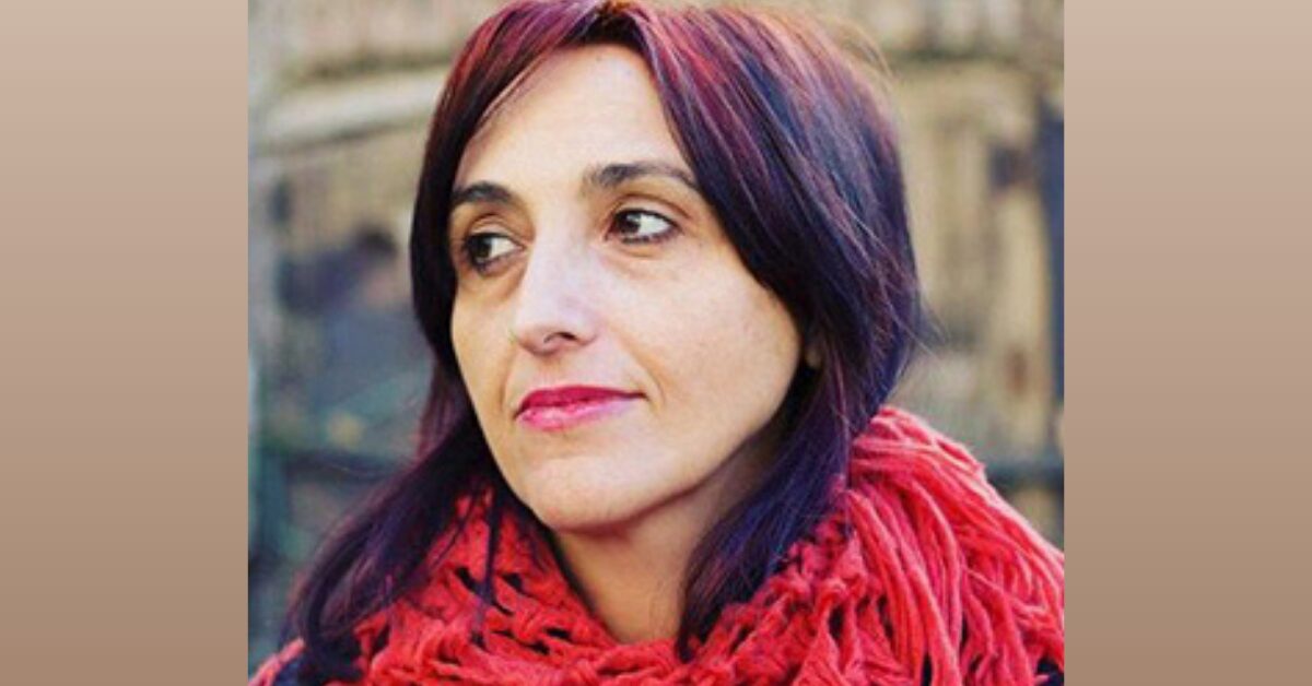 A portrait photo of woman human rights defender Helena Maleno Garzón, a white woman with long hair dyed red and black. She is wearing a bright red scarf around the neck and is looking to the left of the camera.