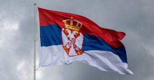 The flag of Serbia flying in the wind against a grey sky background.