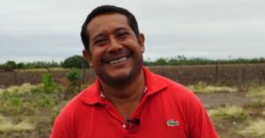 David Hernandez Salazar, a Mexican human rights defender, is smiling warmly in this outdoor photo. He is wearing a red polo shirt with a green Lacoste logo, standing in a field with greenery and a cloudy sky in the background.