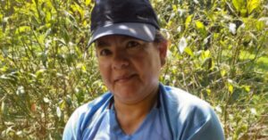 Colombian woman human rights defender Ludivia Galindez is pictured outdoors with green foliage in the background. She is wearing a light blue shirt and a black cap, looking directly at the camera with a gentle smile.