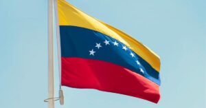 The Flag of Venezuela flying from the top of a pole under a blue sky.