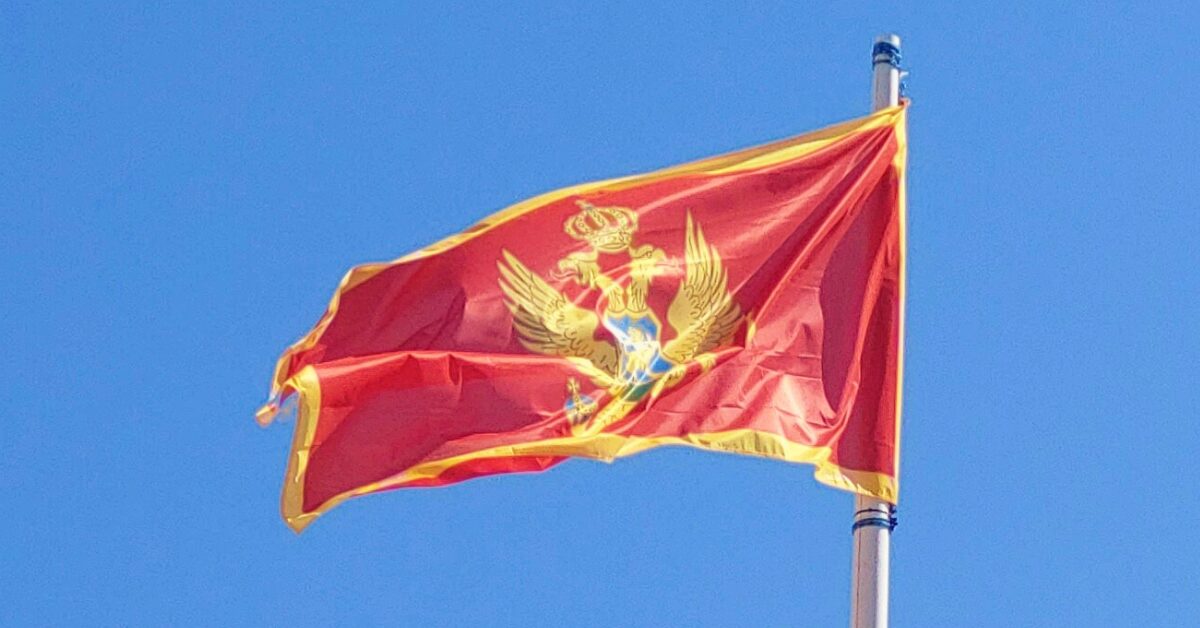 The flag of Montenegro flying in the wind against a blue sky background.