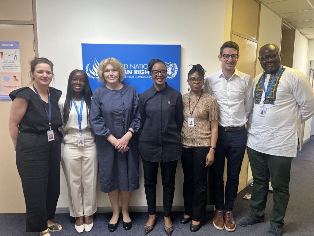 UN Special Rapporteur Mary Lawlor stands alongside staff members of the OHCHR (Office of the High Commissioner for Human Rights) regional office in South Africa. The group is positioned in front of a blue banner with the OHCHR logo. Everyone is smiling and dressed in professional attire.