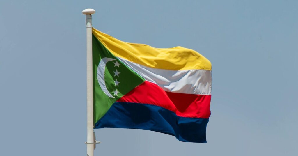 The flag of Comoros flying from the top of a pole against a blue sky background.