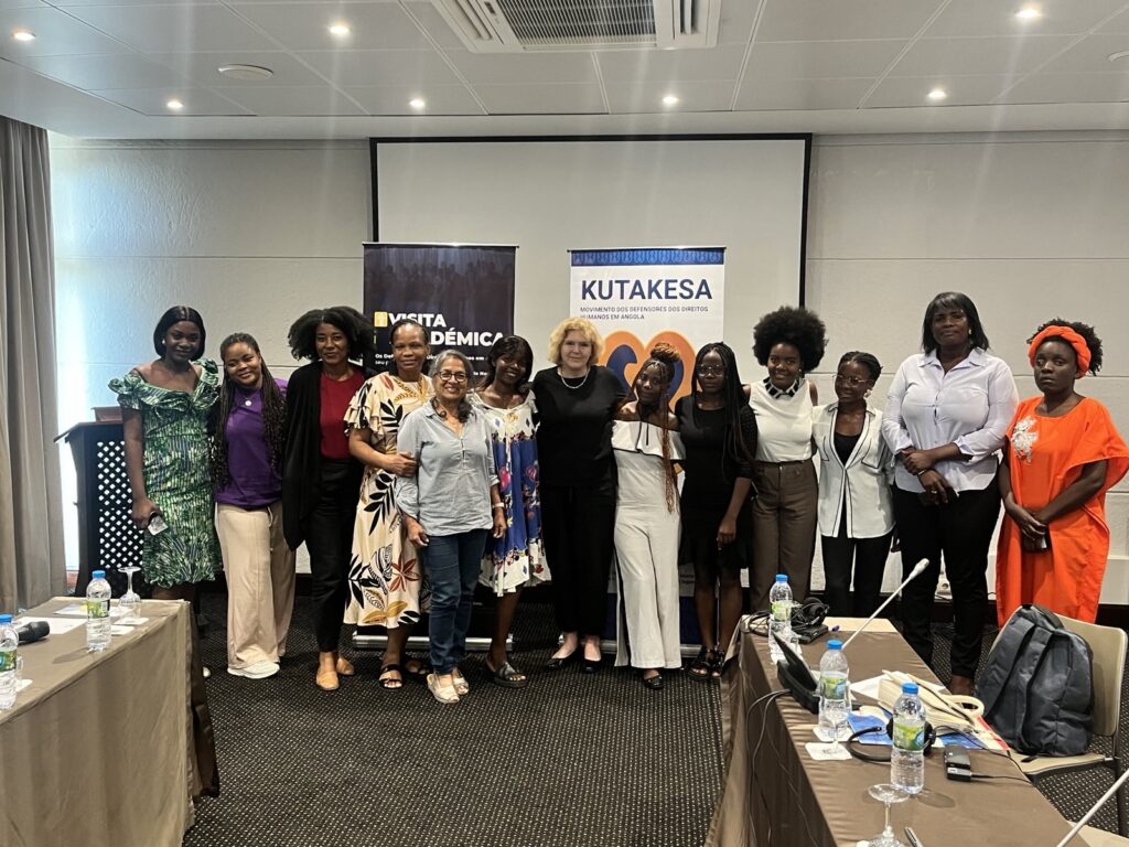 UN Special Rapporteur on Human Rights Defenders Mary Lawlor is standing amongst a group of Angolan women human rights defenders after a meeting. Behind them is a banner from the human rights oranisation Kutakesa.