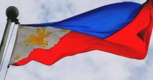 The Philippines flag is flying in the wind at the top of a pole, against a cloudy sky background.