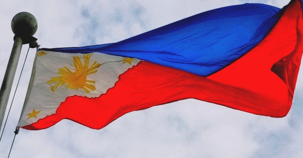 The Philippines flag is flying in the wind at the top of a pole, against a cloudy sky background.