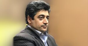 Headshot of Iranian lawyer Taher Naghavi, seen in a close-up. He has dark, wavy hair and is wearing a pinstriped suit jacket. His expression is calm and focused, with a gaze directed slightly away from the camera.