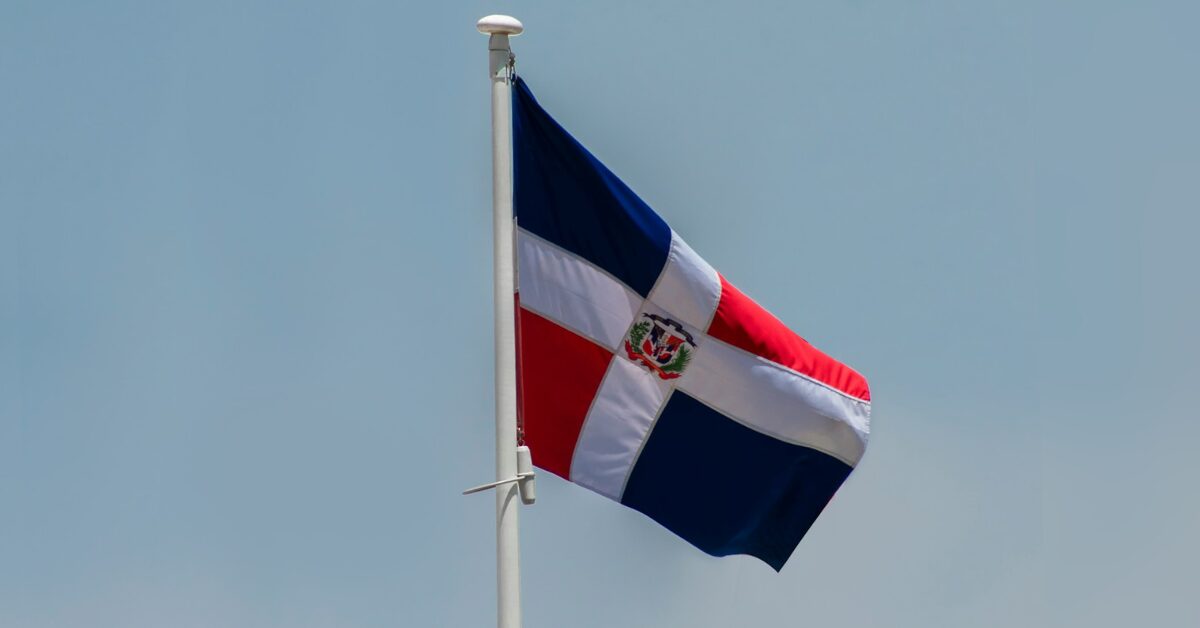 The flag of the Dominican Republic flying from the top of a pole on a bright sunny day.