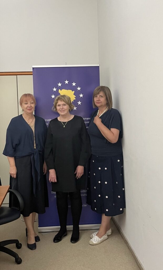 Mary Lawlor, UN Special Rapporteur on human rights defenders, stands with Jasminka Džumhur and Nives Jukić, two of the three Ombudspersons of Bosnia and Herzegovina, in front of a blue banner displaying a map of the country surrounded by stars. They are posing indoors, smiling, in professional attire.