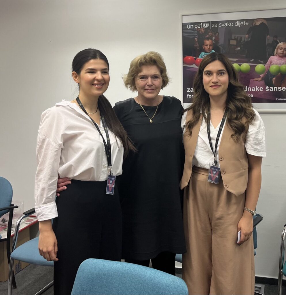Mary Lawlor, UN Special Rapporteur on human rights defenders, stands between two young women human rights defenders, Sara Tuševljak and Sunčica Kovačević, during her official visit to Bosnia and Herzegovina. The three women are smiling and standing in an indoor meeting space, with a UNICEF poster in the background.
