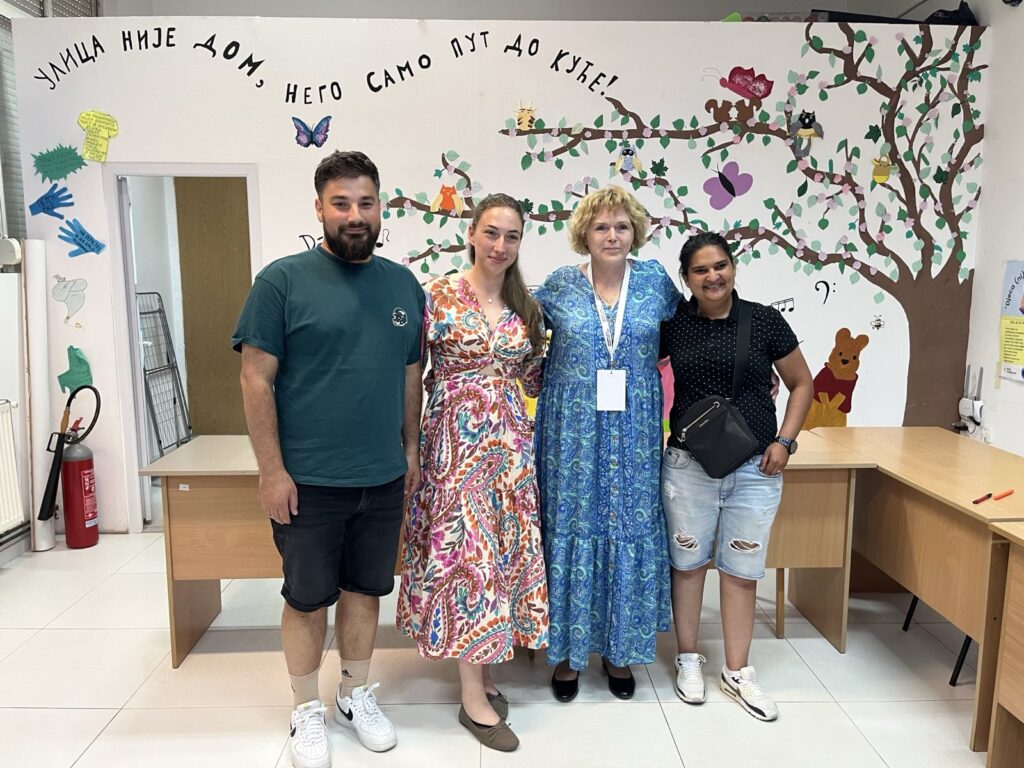 UN Special Rapporteur on human rights defenders Mary Lawlor stands with three human rights defenders working on the rights of the Roma community during her visit to Bosnia and Herzegovina. They are posing together in a brightly decorated room with colourful artwork on the wall behind them, including a tree, butterflies and cartoon animals.