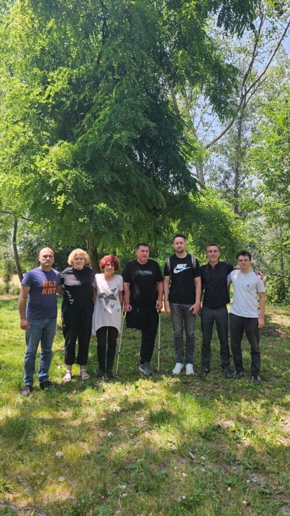 UN Special Rapporteur on human rights defenders Mary Lawlor stands outdoors with a group of environmental human rights defenders and a member of her team during her official visit to Bosnia and Herzegovina. They are smiling together beneath the shade of surrounding trees on a sunny day.
