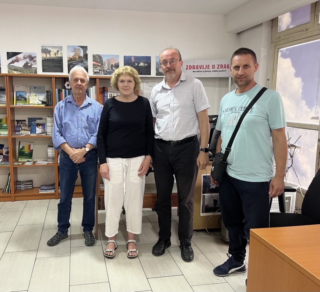Mary Lawlor, UN Special Rapporteur on human rights defenders, stands with three environmental defenders from Eko Forum Zenica, during her official visit to Bosnia and Herzegovina. They are pictured indoors in an office setting, with shelves of publications and photographs of industrial pollution on the wall behind them. A banner reading “Zdravlje u zraku” (Health in the Air) is visible above them.