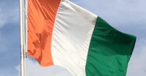 A close up shot of the flag if the Ivory Coast flying in the wind against a blue sky background.
