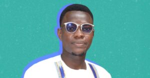 A cutout photo of Alioune Badara Gueye, a young human rights defender from Senegal, on a turquoise colour background. Alioune is wearing tinted glasses and a white shirt with blue and yellow vertical embroidered patterns. He has short hair and a trimmed beard, and is looking directly at the camera with a slight smile.