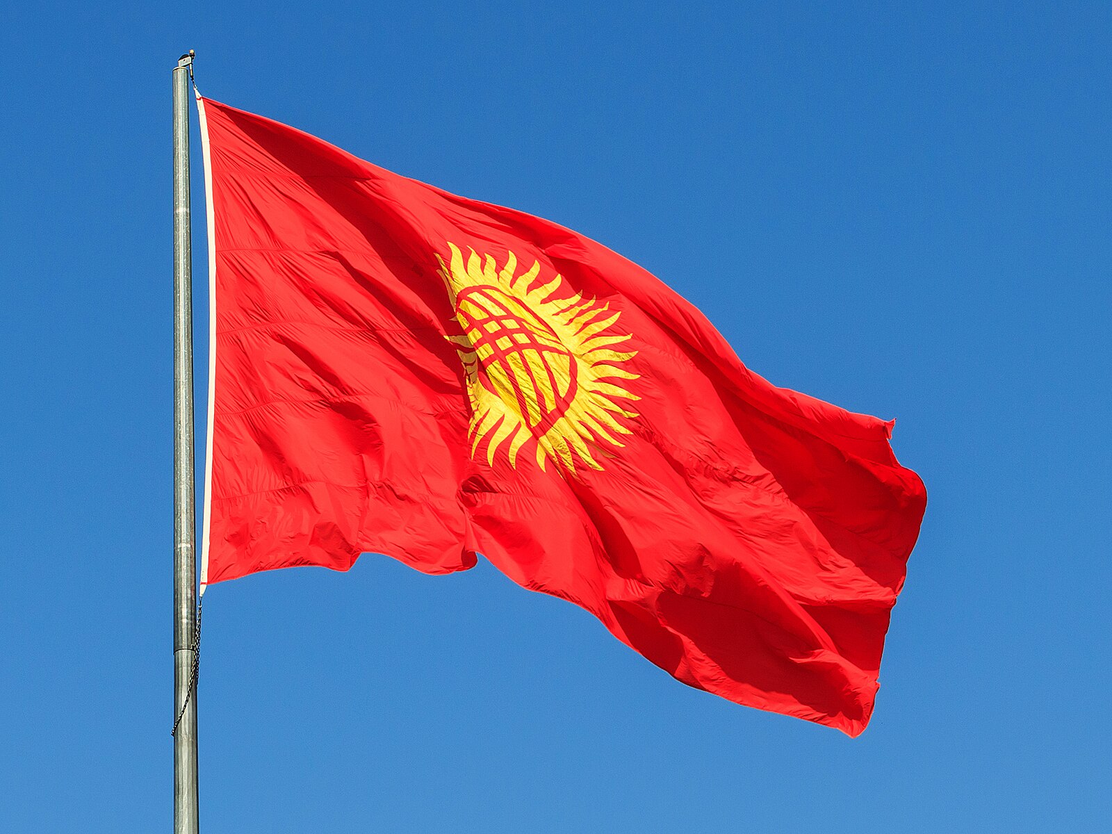 Flag of Kyrgyzstan on a pole against a blue sky
