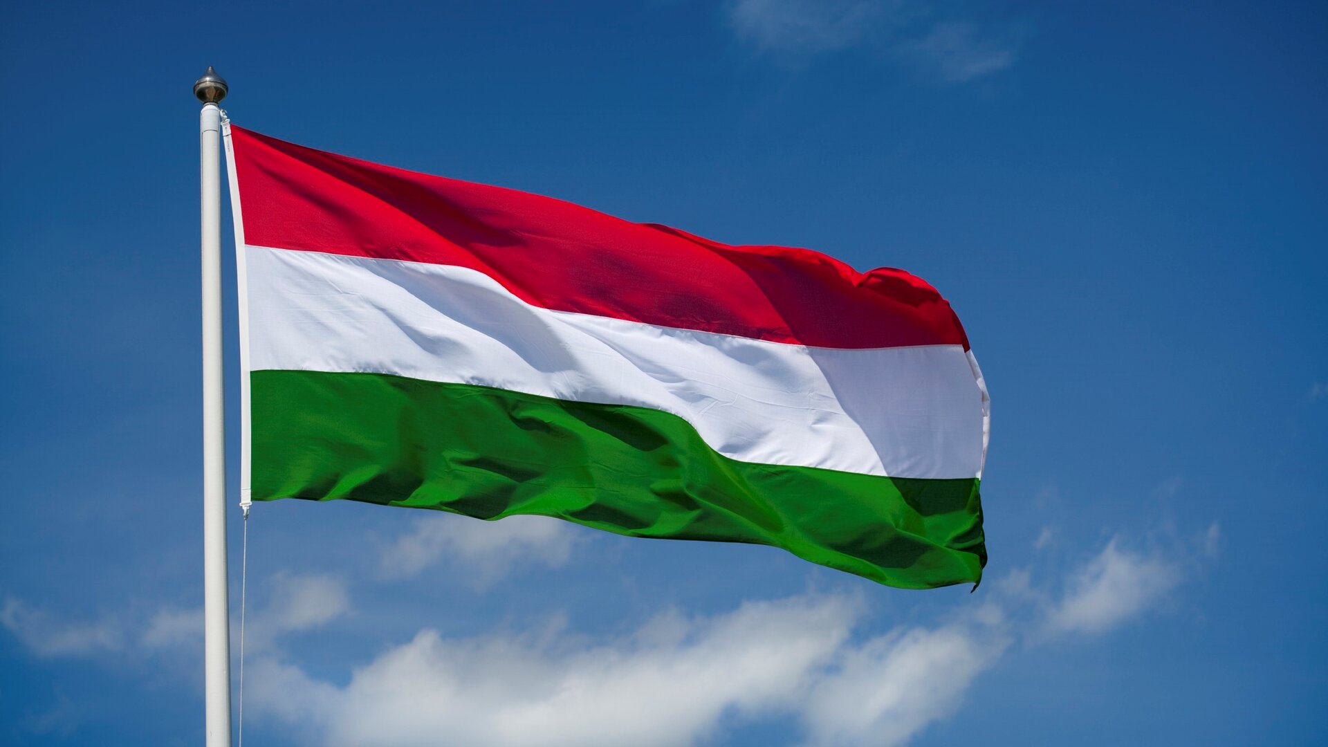 The flag of Hungary flying in the wind against a blue sky background.