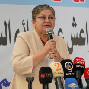The woman human rights defender and feminist Yanar Mohammed, standing in front of a row of microphones holding a microphone herself